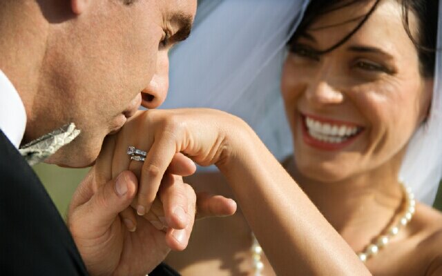 Groom kissing hand of smiling bride.
